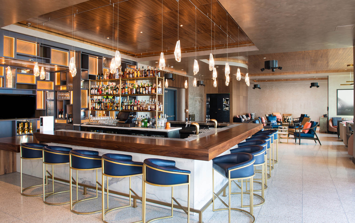 A modern bar with a wooden counter, blue stools, and gold accents.